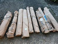 Nine paper-wrapped bundles of wood laying on pavement, showing size variety and packaging