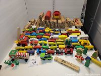 Overall view showing wooden tracks, multiple colorful wooden cars and trains, red tunnel and yellow bridge pieces, assorted accessories, and storage tote