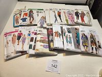 Photo showing 18 assorted sewing pattern envelopes from McCall's, Simplicity, New Look, Butterick brands, featuring various women's clothing styles including dresses, pants, tops, jackets.