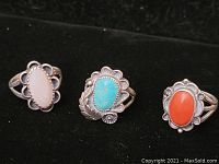 Three Native American sterling silver rings with turquoise, white shell, and coral stones on black background.