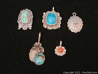 Top view of five Native American sterling silver pendants showing turquoise, coral, and floral designs on black background.