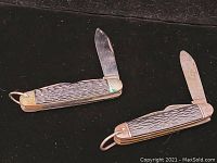 Two Camillus pocket knives shown with blades open, placed on a dark surface.