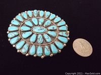 Front view of a large Native American sterling silver and turquoise brooch next to a quarter for size reference.