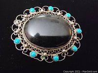 Front view of vintage sterling silver brooch with large black oval stone and turquoise embellishments on silver filigree.