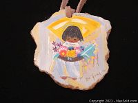 Photo of wooden pendant with colorful hand-painted image of a girl holding flowers on a black background.