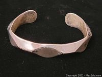 Sterling silver cuff bracelet showing the wave pattern design on black background.