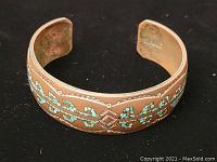 Copper cuff bracelet with turquoise inlay and engraved design, open ended, lying flat on dark surface.