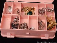 Pink plastic storage case with subdivided compartments containing assorted jewelry pieces.