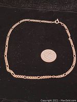 Photo of a single sterling silver necklace on a black background with a quarter coin for size comparison.