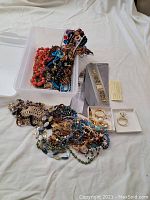 Full view of collected jewelry including beaded necklaces, rings, and watches displayed on white cloth