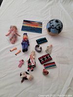 Lot contents on white cloth including dolls, pottery, woven pieces, loose parts, and painted card