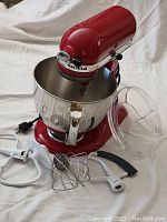 Overall view of red mixer, stainless bowl, pouring shield and attachments on white background
