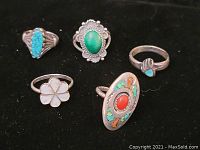Five Native American sterling rings displayed on black background. Rings show various stones including turquoise, coral, malachite, and shell inlay. A quarter is placed for scale.