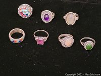 Photo of six sterling silver rings with various gemstone and enamel designs, arranged on black background to show details
