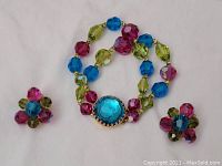 Front view of bracelet and pair of earrings laid flat showing colorful faceted beads in blue, pink and olive green with blue centerpiece on bracelet