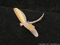 Dragonfly brooch showing top and side view with gold-tone and silver textured wings on black background.