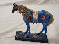 Blue horse figurine decorated with colorful handprints and fringe saddle, viewed from left side