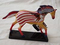 Side view of one horse figurine showing red, white, blue stars and stripes with an eagle motif and glossy finish on black base.