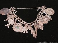 Silver charm bracelet on black background showing all charms and safety chain