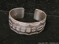 Front view of silver cuff bracelet showing detailed engraved decorative patterns and scalloped edges.