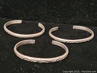 Three sterling silver cuff bracelets shown from above, with embossed patterns visible.