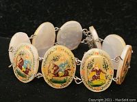 Close-up of oval tile segments showing hand-painted Asian figures and nature motifs, linked by metal chains in bracelet form