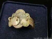 Close-up of the decorative top of the silver ring with three small dangling round discs and engraved floral or scroll design.