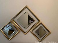 Four framed mirrors arranged in a diamond pattern on a wall. The mirrors have gold-tone frames with beveled edges.