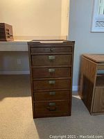 Full view of a wooden older style file cabinet with six drawers, metal handles, and label holders.