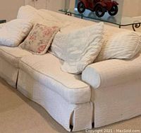 Front view of a three-seat sofa with slipcover and multiple cushions in a light color.