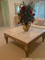 Front angle view of large square coffee table with beige stone top and carved wooden legs, displaying decorative details.