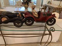 Glass sideboard with clear glass top and two lower glass shelves supported by a gold metal curved frame. Model cars placed on top for size reference only, not included.