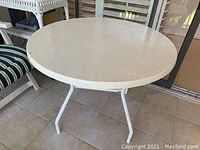 Round weathered white patio table on a tiled patio.