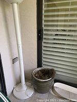 Photo of a green ceramic pot placed on the floor near a white lamp and glass door with blinds.
