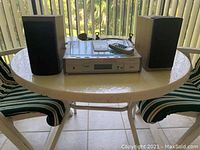 Silver CD player with front display and controls on top, two black speakers on either side, and a remote control placed on the player.