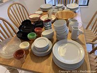 Photo of assorted dishes including various plates, bowls, mugs, and pitchers arranged on a wooden dining table.