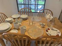 View of the set of dishes arranged on a wooden table including plates, mugs, pitchers, and glass serving pieces.