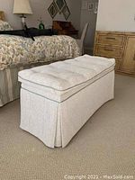 Photo of an upholstered rectangular bench with tufted cushioned top and pleated skirt base in a bedroom setting.