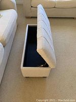 Side view of the light fabric upholstered storage bench with the hinged lid open showing interior storage space.