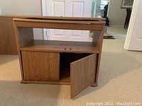 Front view of wooden TV table showing one cabinet door open, open middle shelf, and flat top surface.