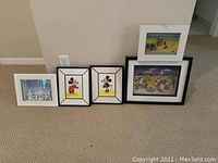 Photo showing five framed pictures along a wall on carpet, including two Mickey Mouse images, beach scene, cartoon picnic, and building close-up picture.
