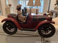 Red vintage style car figurine with female driver in a hat and dress, displayed indoors.
