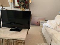 Photo showing a black flat screen television on a marble-top table in a living room setting with sofa and lamps nearby.