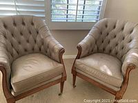 Pair of beige leather armchairs with wooden frames.