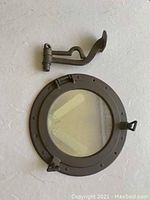 Nautical style round porthole window with latch and attached hardware, metal construction, dark finish, glass in center
