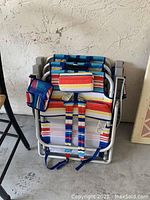 Two foldable beach chairs stacked together showing aluminum frames and colorful striped fabric seats, with attached padded headrests and carrying straps.