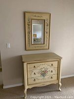 Front view of cream colored dresser with hand-painted floral designs and matching wall mirror above it.