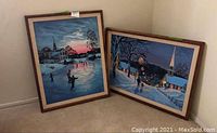 Two framed winter landscape paintings resting against the corner of the room on carpet. One vertical, one horizontal. Display of lot contents and framing.