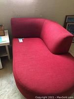 Photo showing red fabric one arm chaise lounge with curved shape.