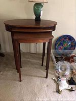 Front view of the three nesting tables showing the large oval table on top and smaller two rectangular shape tables underneath next to colorful decorative items.